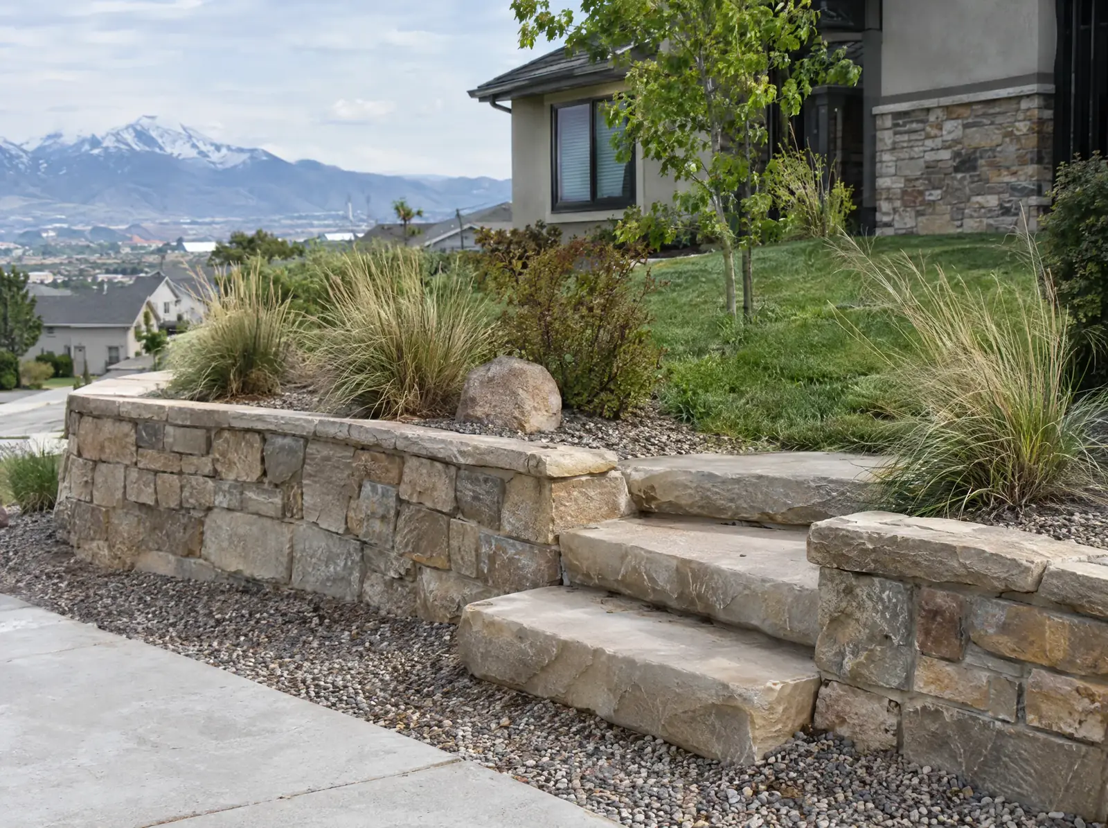 Natural stone retaining wall with broad steps, ornamental grasses planted above it and a gravel border below.
